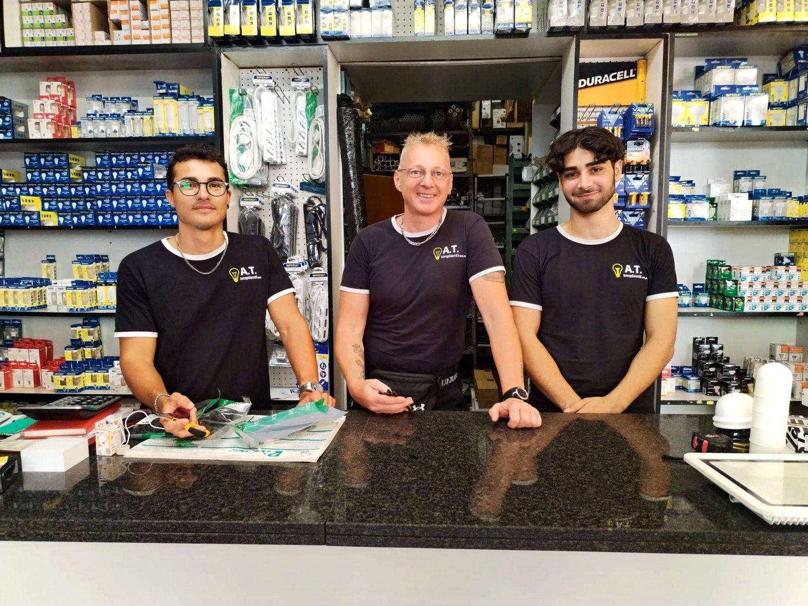 Lo staff del negozio A.T. Impianti in Via Tunisi 40-42 — tre ragazzi dietro il bancone pronti ad accogliere i clienti
